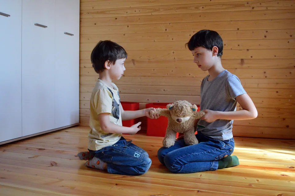 Two children sitting face to face on a wooden floor.