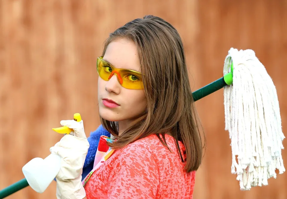 A woman holding cleaning supplies and a mop.