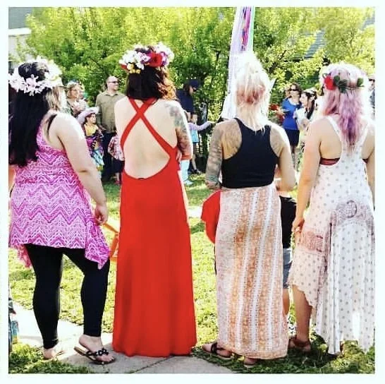 A group of people wearing dresses and floral wreaths outdoors.
