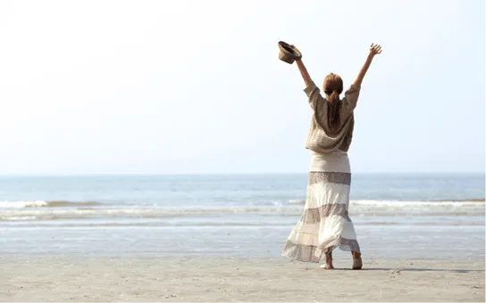 A woman standing in ocean surf with her arms raised.