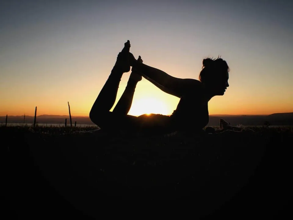 A woman practicing yoga in silhouette at sunset.