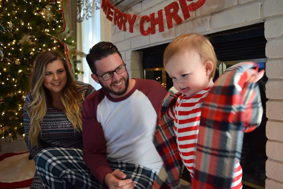 Two adults and a child seated beside a Christmas tree.