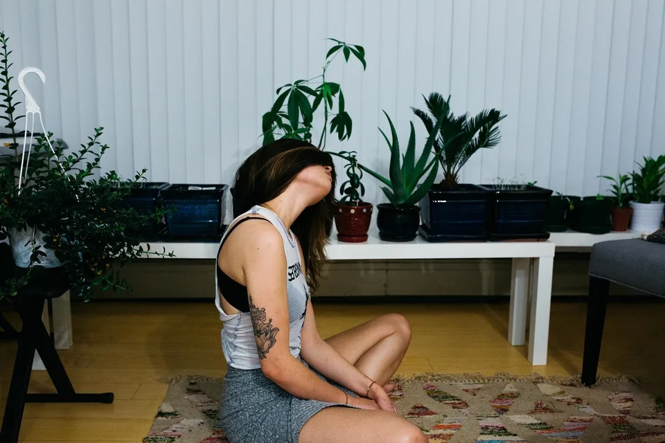 A woman sitting on the floor in a plant-filled room.