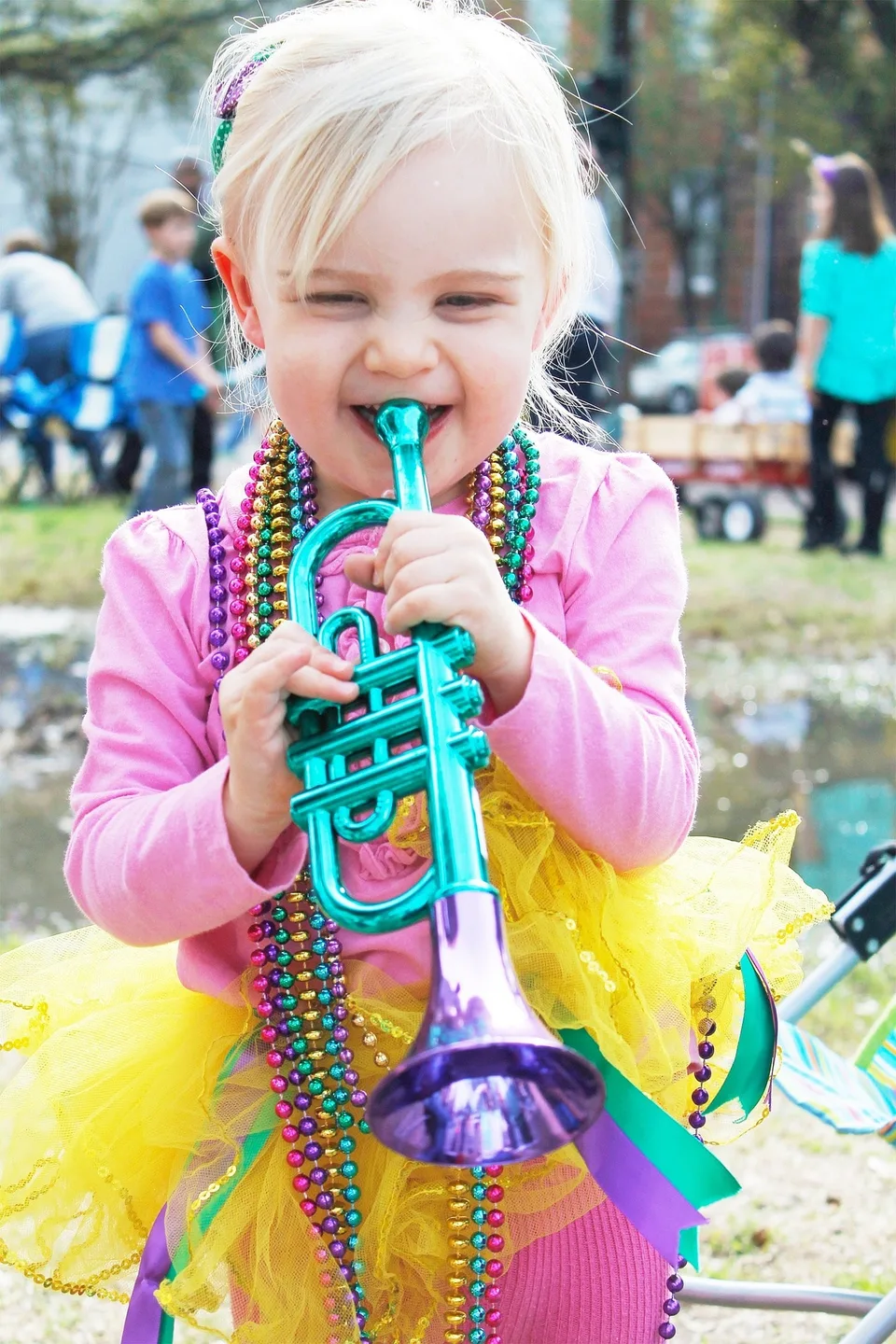 A child wearing colorful beads and holding a toy trumpet.