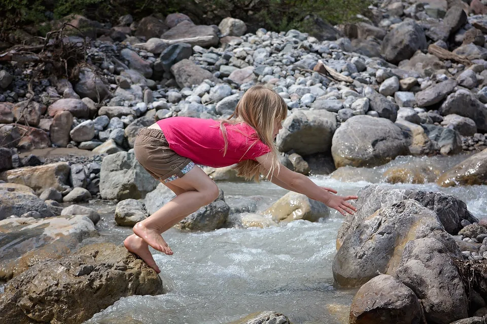 A woman stepping between rocks beside running water.