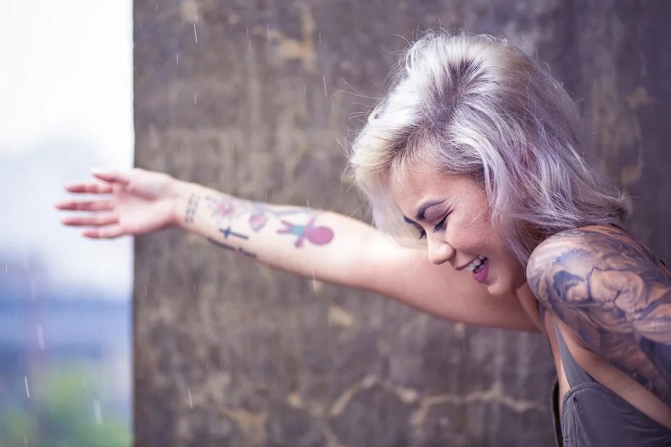 A woman with tattooed arms leaning forward outdoors.