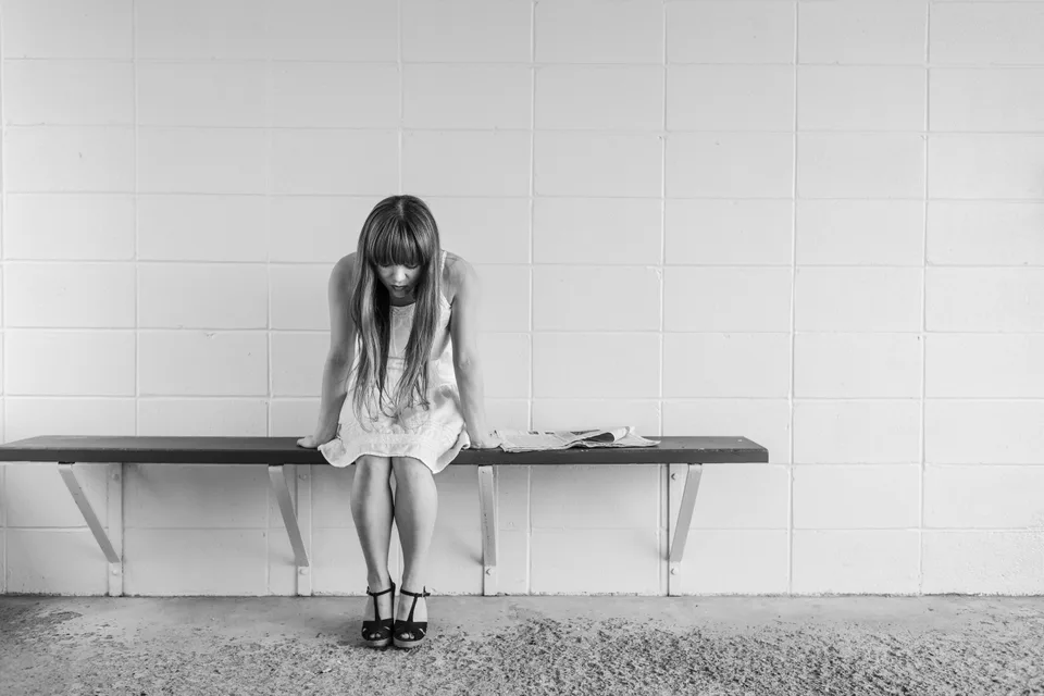 A woman seated alone on a bench against a tiled wall.